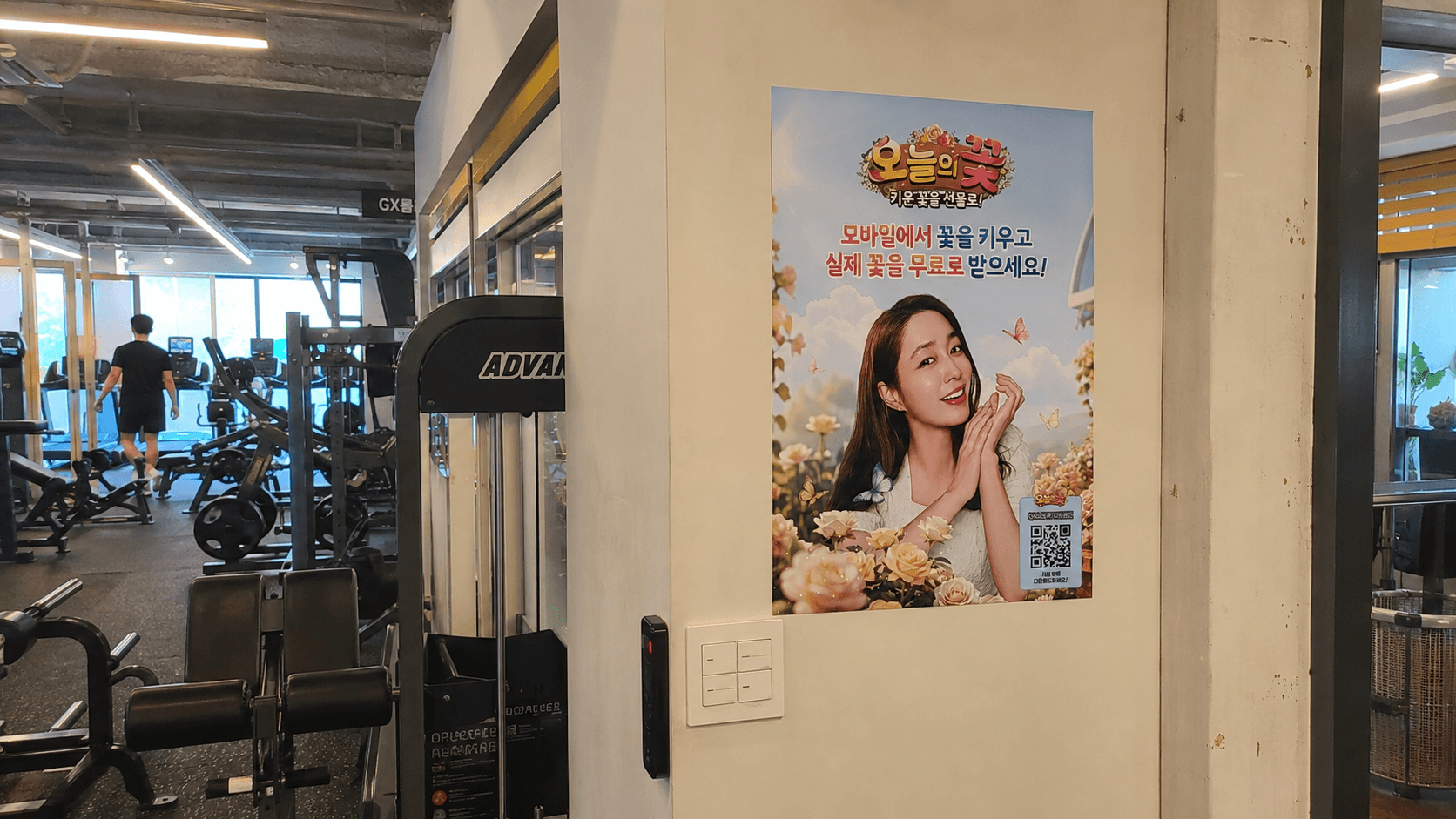 헬스장 출입 동선 옆 벽에 이민정 포스터가 붙은 모습